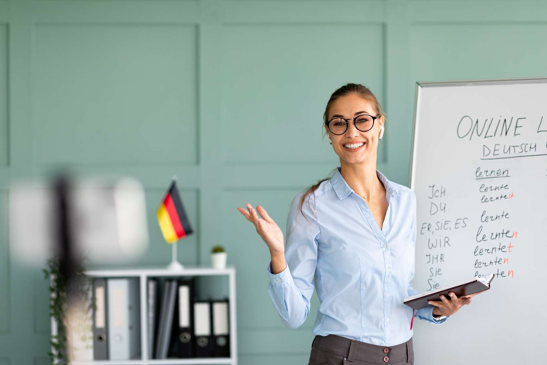Online languages school. Friendly female tutor giving German lesson on internet, using smartphone and explaining grammar