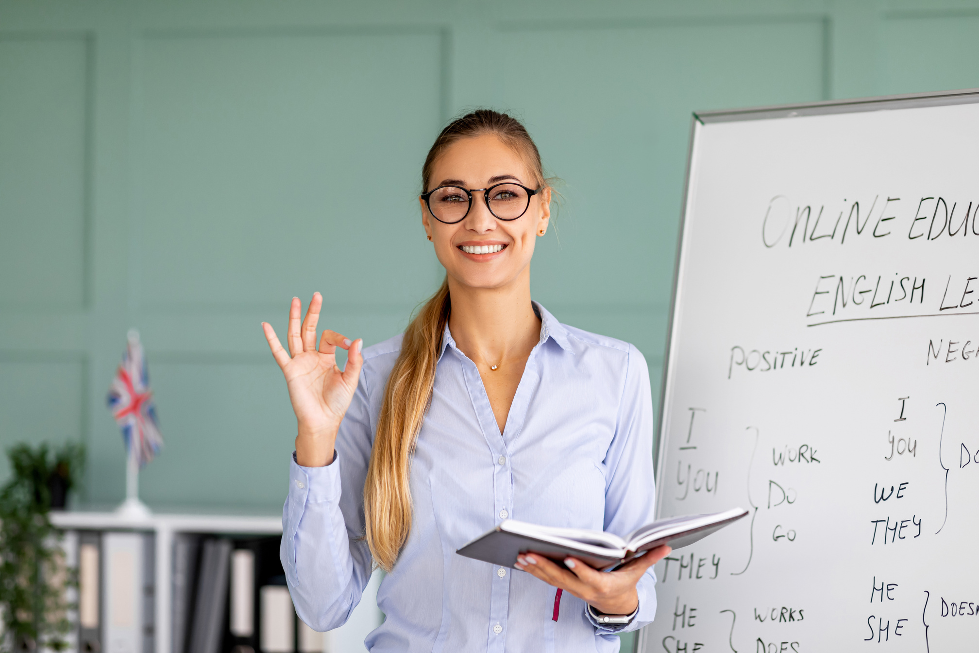 Positive female tutor giving English lessons online, recommending foreign languages school, showing ok gesture